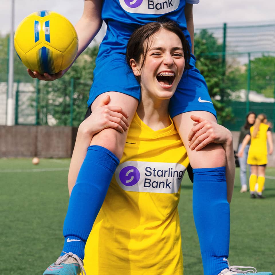 Girl carrying another one with ball on her shoulders