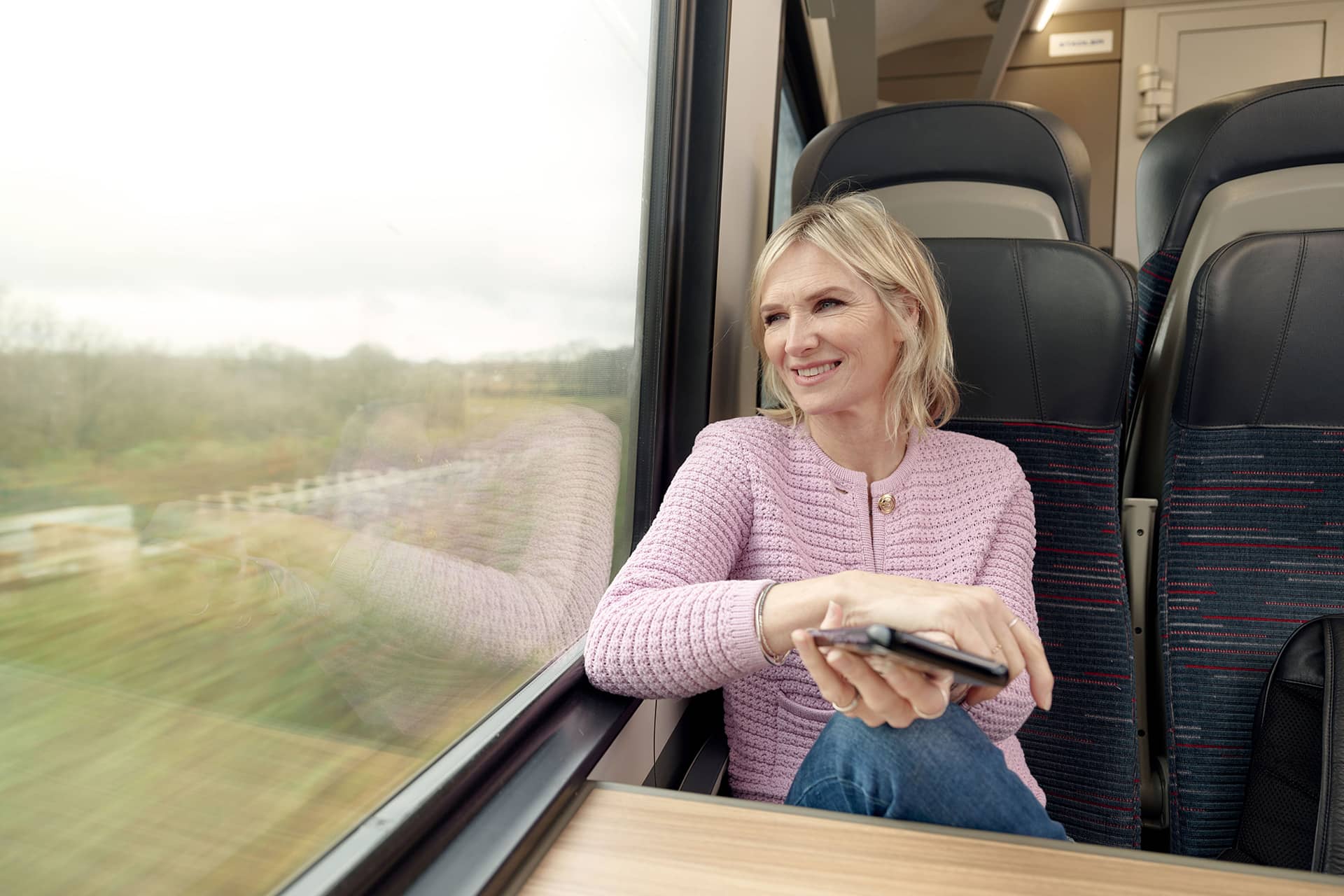 Woman looking out of the window on train holding the mobile phone